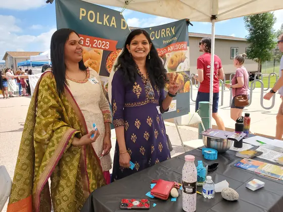 Two organisers in traditional dress beside the Polka Dots & Curry festival banner