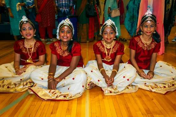 Young dancers in red and gold costumes seated together after performing