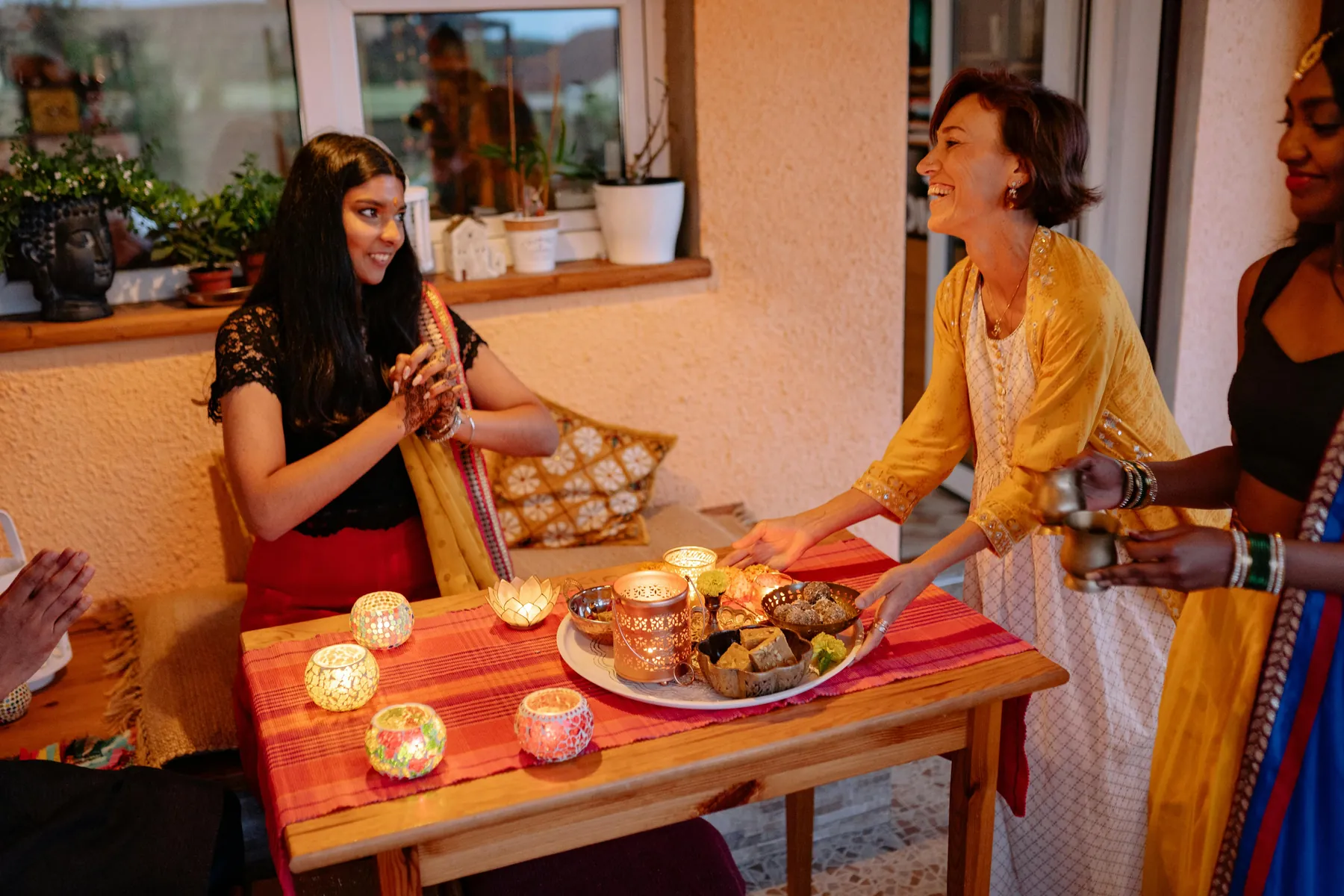 Friends gathered around a table of Indian sweets and lit diyas